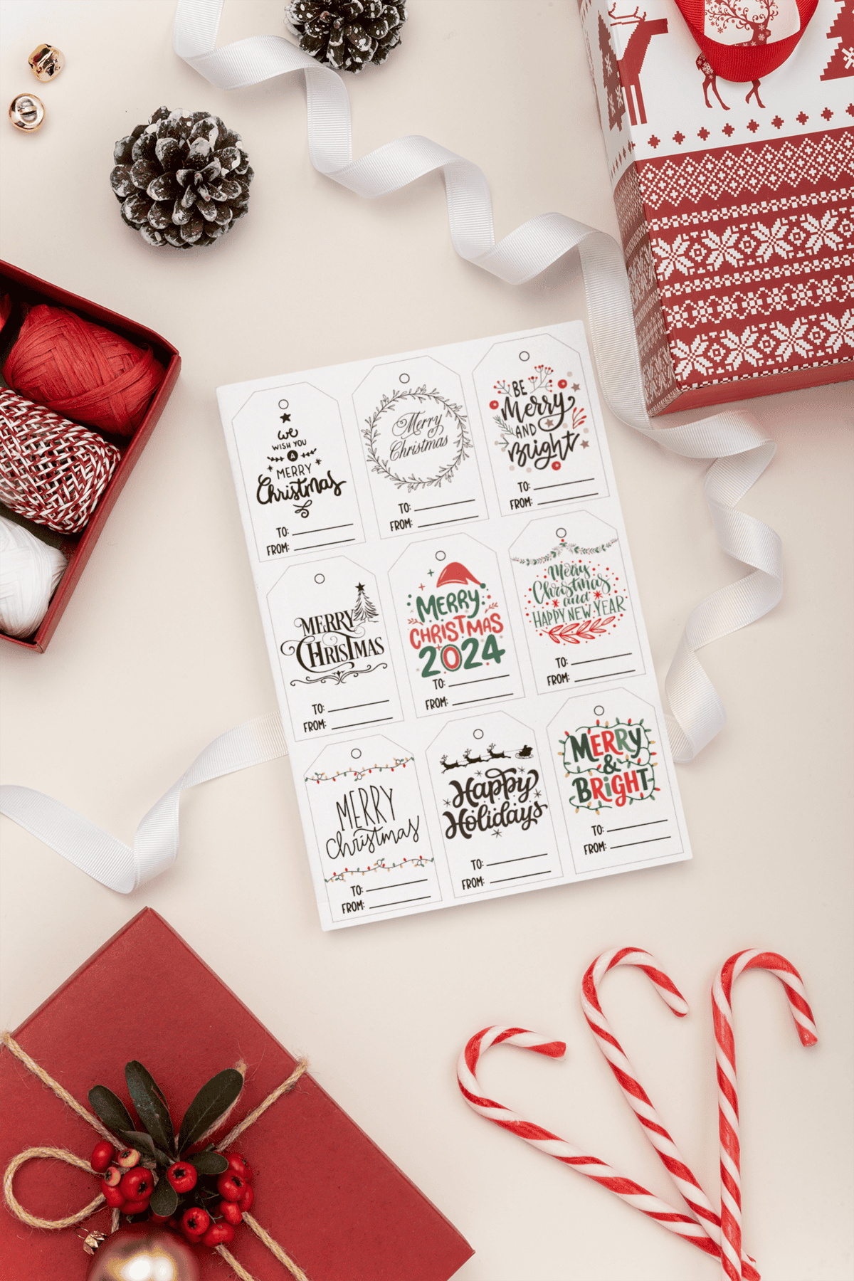 Collection of Christmas gift tags with festive greetings like 'Merry Christmas 2024' and 'Happy Holidays,' arranged alongside holiday decorations like red yarn, candy canes, and wrapped presents.